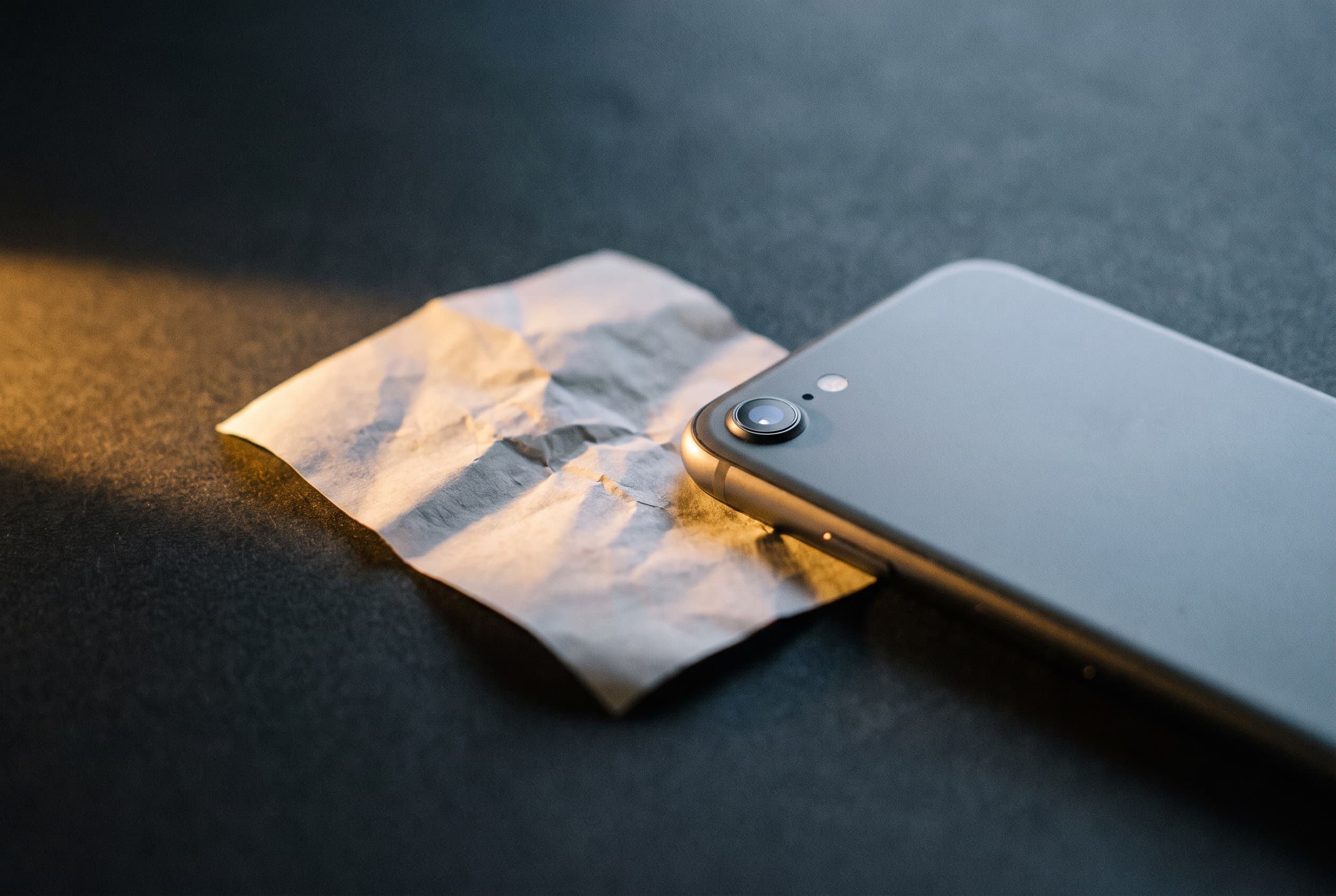 A phone lying on a dark surface next to a paper receipt lit by a warm shaft of light.